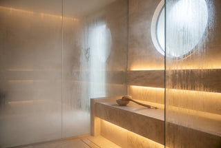Modern tiled steam room filled with steam, condensation on the glass and warm LED bench lighting