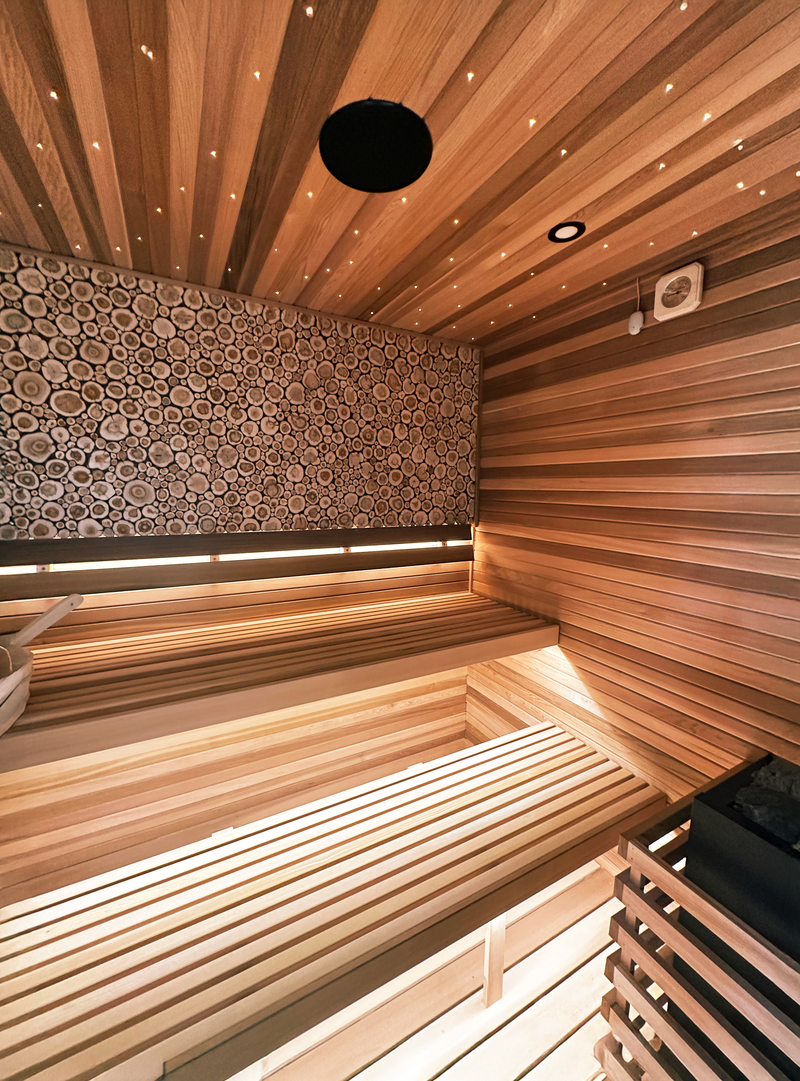 A finished Cedro custom sauna with lit benches and a log-round accent wall